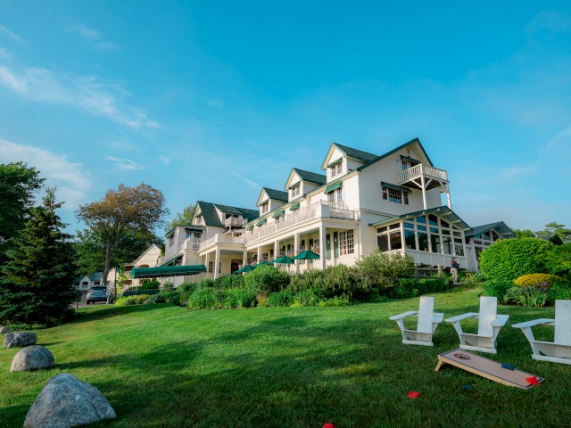 The Main Inn with a green lawn, trees, white chairs, and a cornhole game setup, all under a clear blue sky.