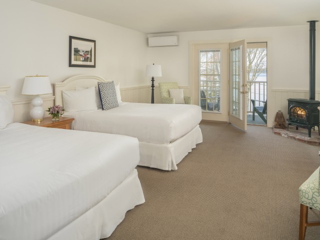 This image shows a well-lit hotel room with two beds, a TV, a wooden dresser, a chair, and a door leading to a balcony.