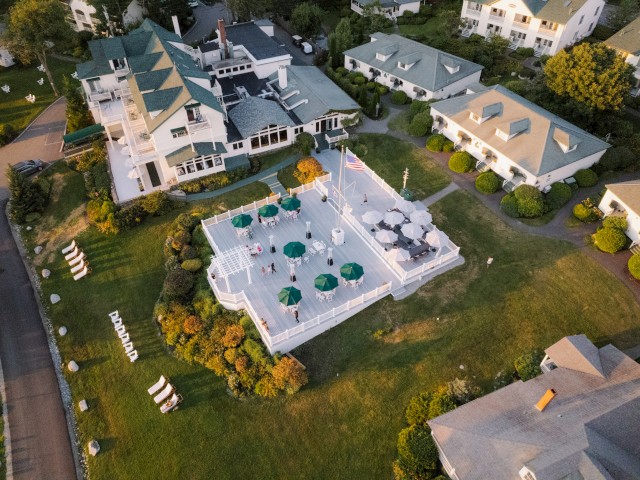 An aerial view of a picturesque outdoor terrace with umbrellas and chairs surrounded by charming buildings and well-maintained landscaping.
