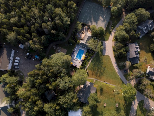 The image shows an aerial view of a residential area with houses, a swimming pool, a tennis court, and surrounding trees.