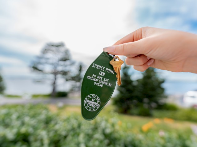 A hand holds a green keychain with keys. The keychain reads 