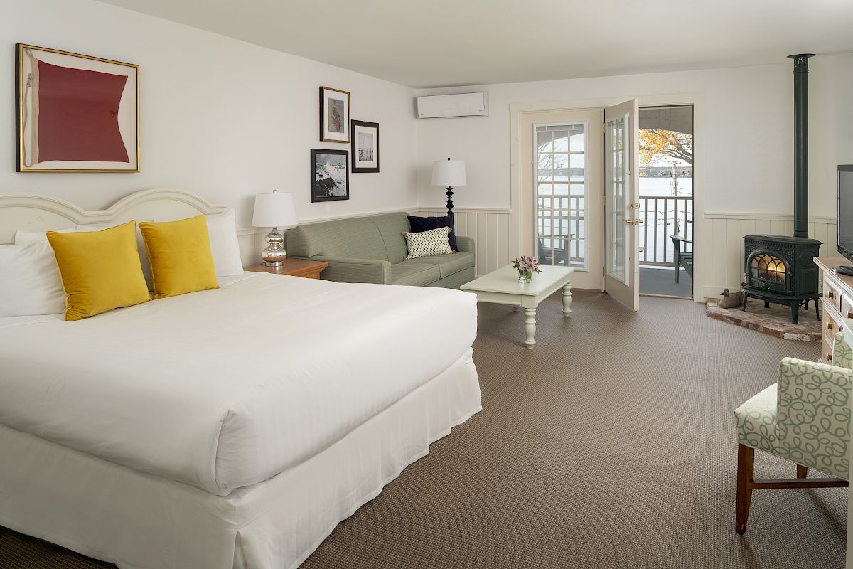 A cozy bedroom with a large bed, yellow pillows, sofa, coffee table, stove, and balcony with a view, decorated with framed pictures ending the sentence.