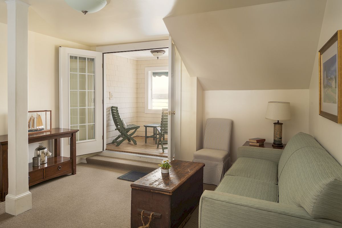 This image shows a cozy living room with a sofa, a wooden chest, a table, and a doorway leading to a small, enclosed porch.