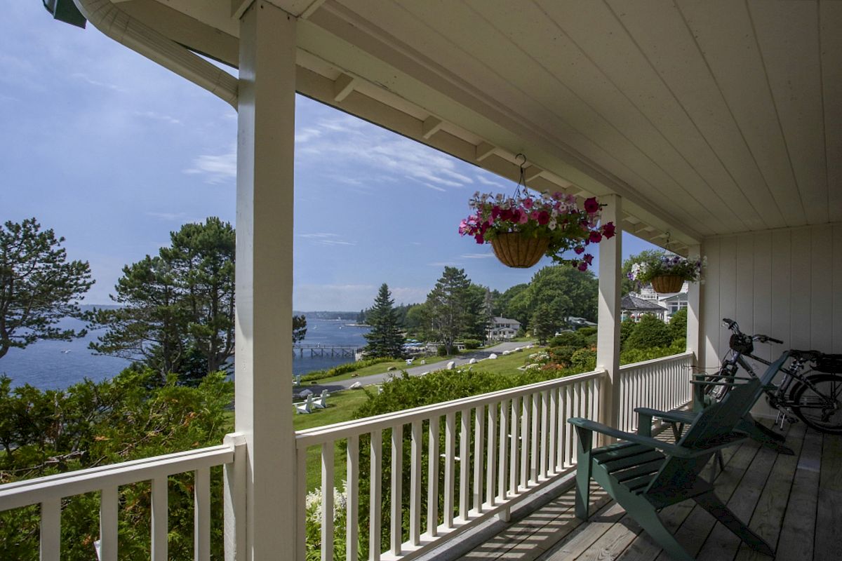 A porch overlooks a scenic view with trees, water, and houses in the distance; chairs and a bicycle are on the porch.