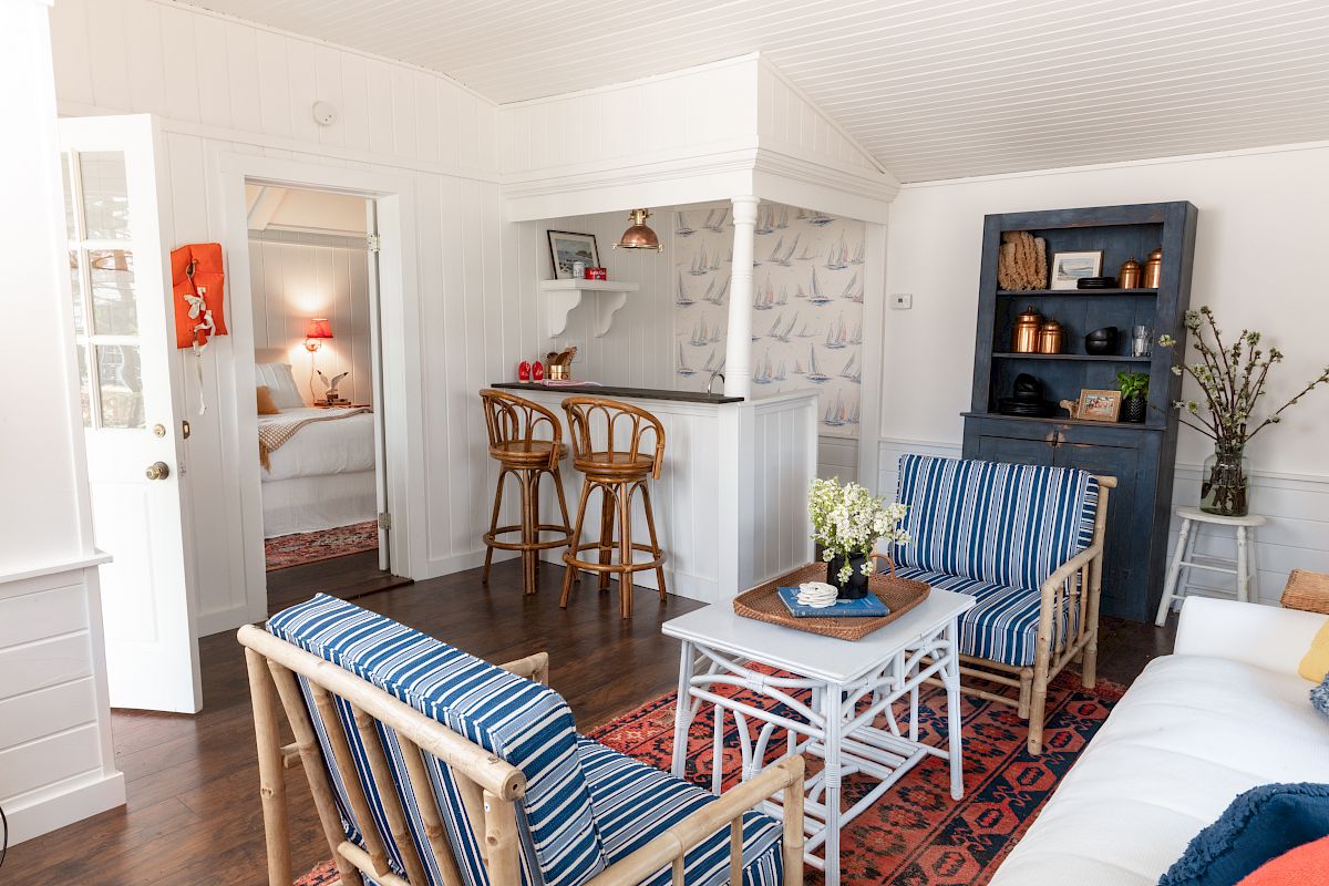 A cozy living room with nautical-themed decor, featuring striped furniture, a coffee table, and a small bar area with stools. End of sentence.
