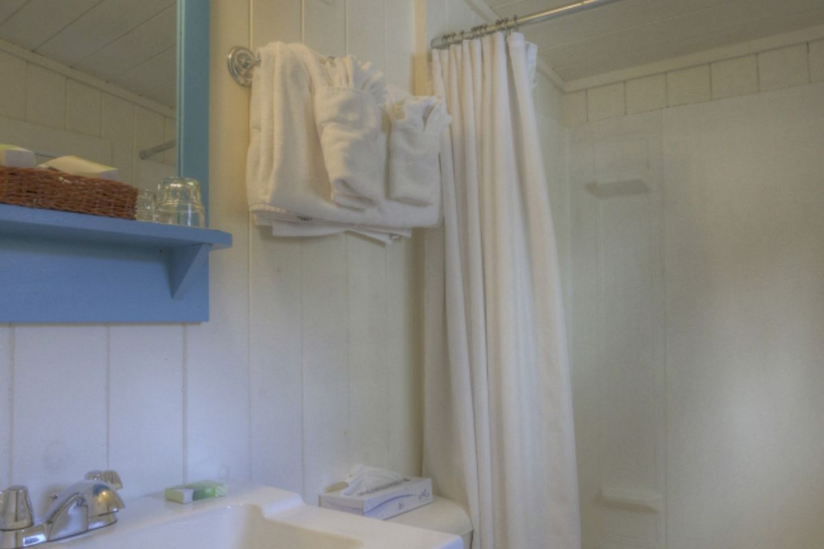 This image shows a small bathroom with a sink, mirror, and toilet on the left, a bath/shower combination with a curtain on the right, and towels hanging.