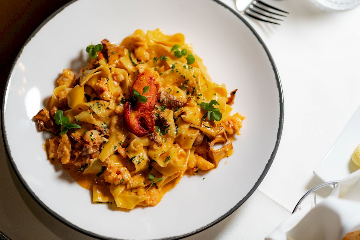 A plate of pasta with a creamy sauce, garnished with herbs, and served on a white tablecloth with silverware in the background.