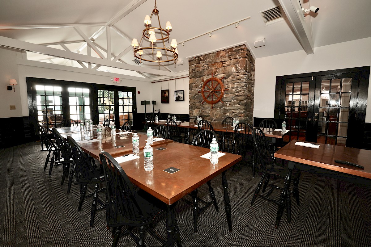 A conference room with wooden tables, chairs, water bottles, and stationery, decorated with a stone wall and a decorative ship wheel.