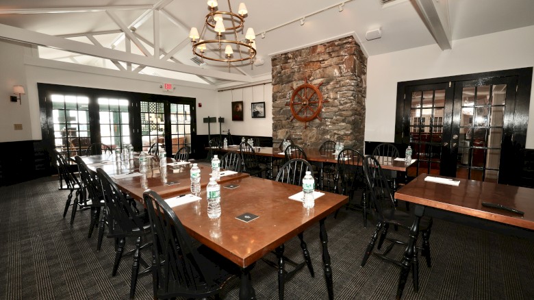 A conference room with wooden tables, chairs, water bottles, and stationery, decorated with a stone wall and a decorative ship wheel.