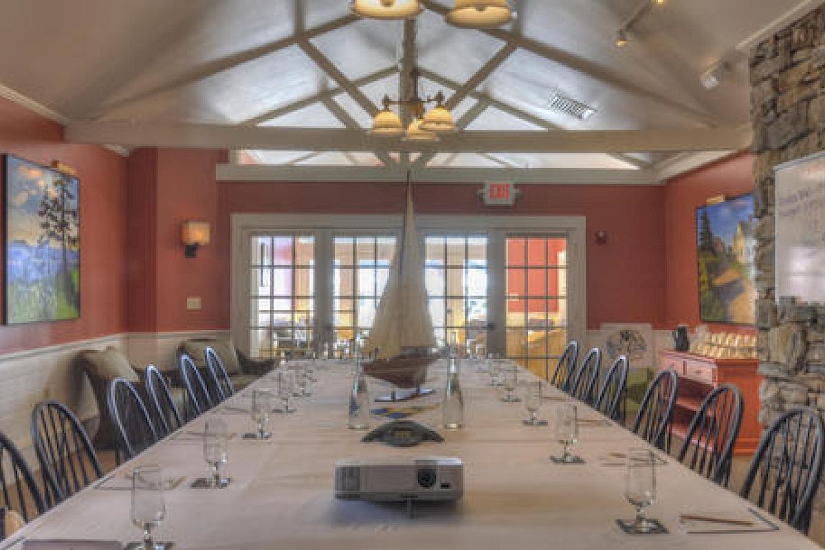 The image shows a conference room with a long table, chairs, a projector, water glasses, art on the walls, and a large window at the end of the room.