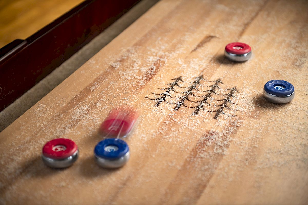 The image shows a game of table shuffleboard with red and blue pucks sliding on a board dusted with powder. Ending the sentence.