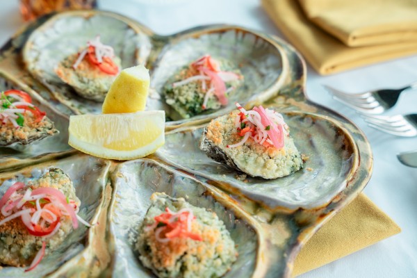 A platter with stuffed oysters, garnished with herbs and sliced onions, accompanied by lemon wedges on a decorative shell plate.