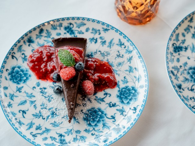 A slice of chocolate cake with berries and a drizzle of sauce on a floral plate.