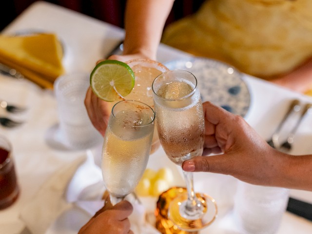 Three people toasting with champagne glasses at a dining table set with plates, cutlery, napkins, and a candle.