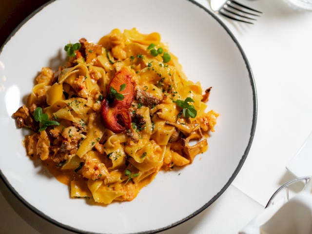 A plate of pasta with a creamy sauce, garnished with herbs and possibly seafood, presented on a table setting with cutlery.