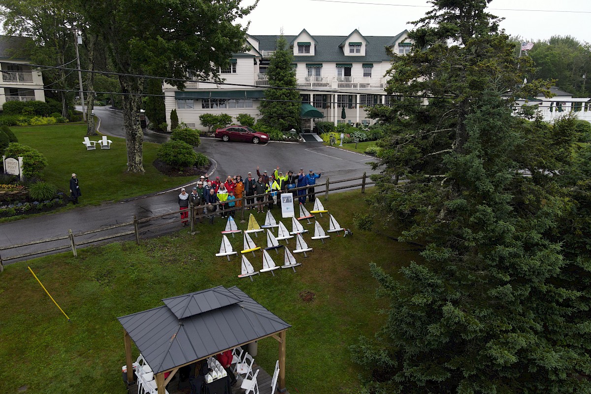 A group of people stands near triangular structures outdoors, with a white building and trees in the background.
