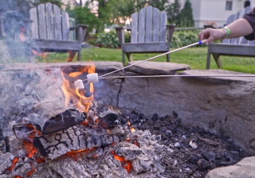 Two marshmallows being roasted over a campfire with chairs and greenery in the background.