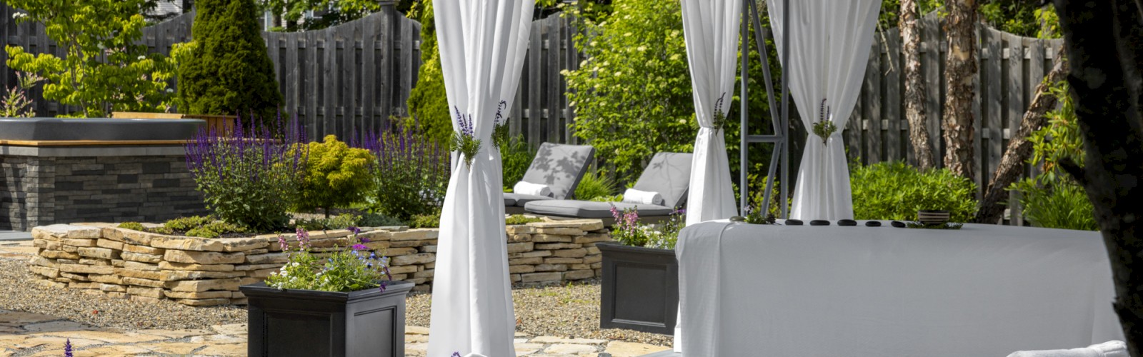 This image shows a serene garden with a gazebo, white curtains, lounge chairs, potted plants, and a bottle of water on a table, creating a relaxing space.