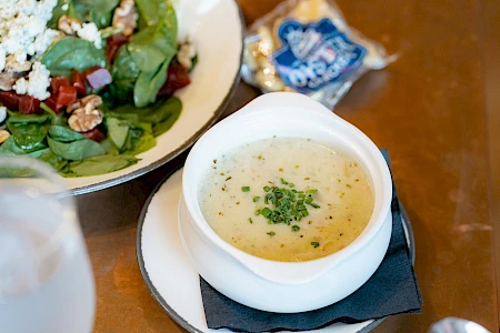 A bowl of creamy soup garnished with chives, a salad with greens and walnuts, and a packet of oyster crackers on the side.