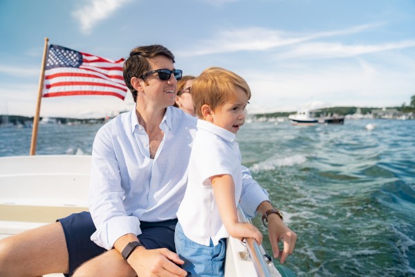 A person and child are on a boat with an American flag, enjoying a sunny day on the water.