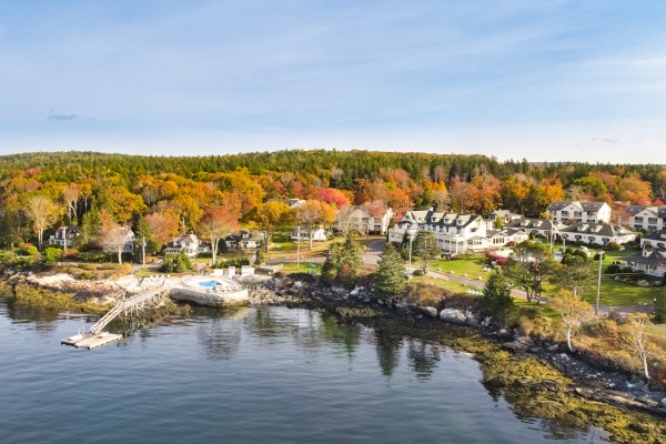 A coastal village with colorful trees, houses, a dock, and calm water reflecting the serene surroundings.