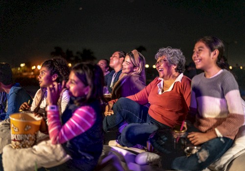 People sitting outdoors, smiling and watching something at night, with buckets of popcorn.