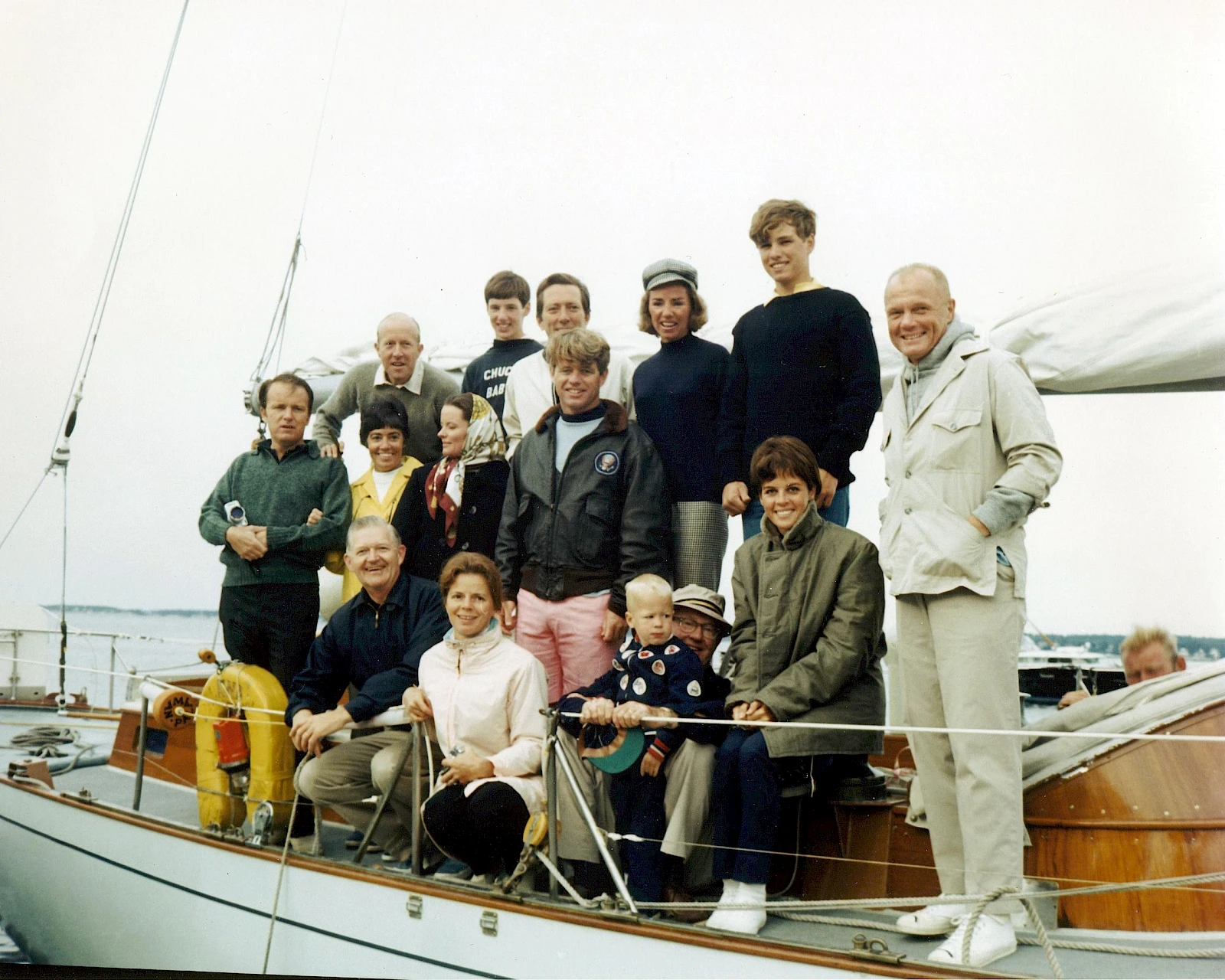 A group of people posing on a sailboat by the water, dressed in casual and nautical attire.