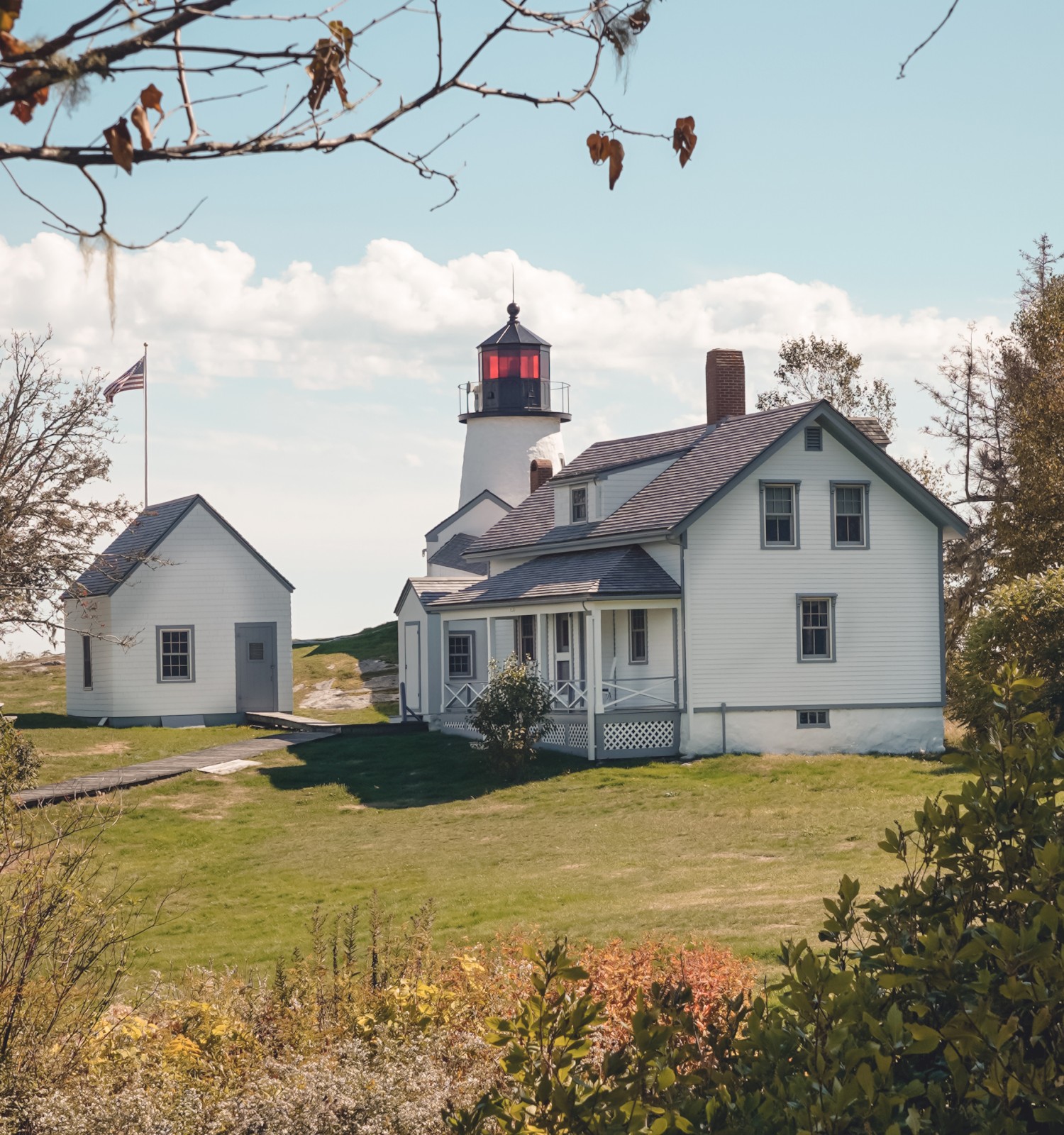A picturesque lighthouse and house on a grassy landscape with autumn leaves and blue sky in the background.