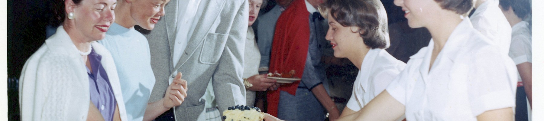 A crowded bake sale or reception with people serving cake to a line of customers, vintage vibe and uniforms.