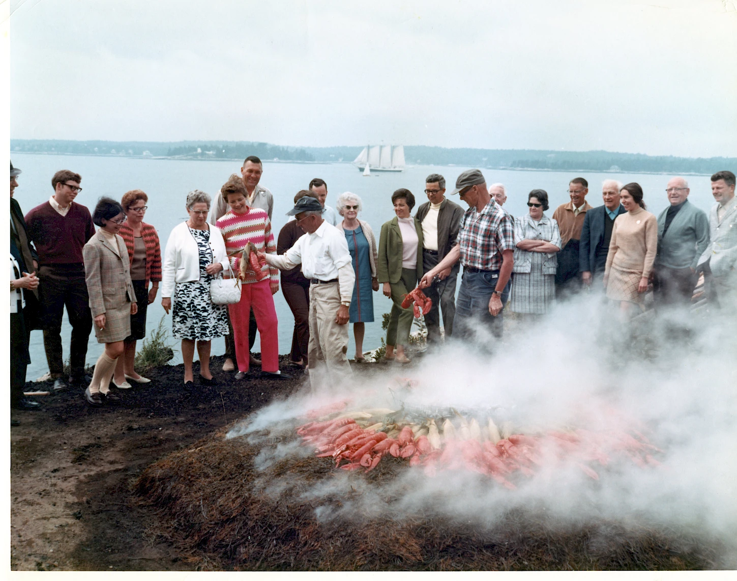 A group of people stands by a volcanic crater or smoke-lit ground, observing a glowing ember or lava pool from a distance.