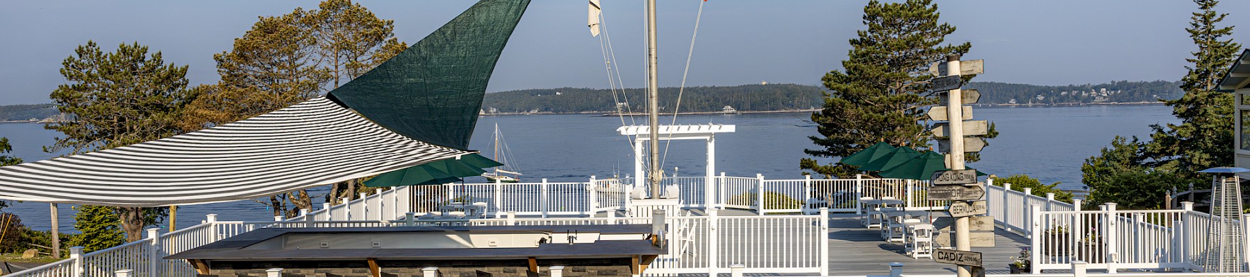 A scenic lakeside patio with white fencing, flags, outdoor seating, and a view of the water under a blue sky.